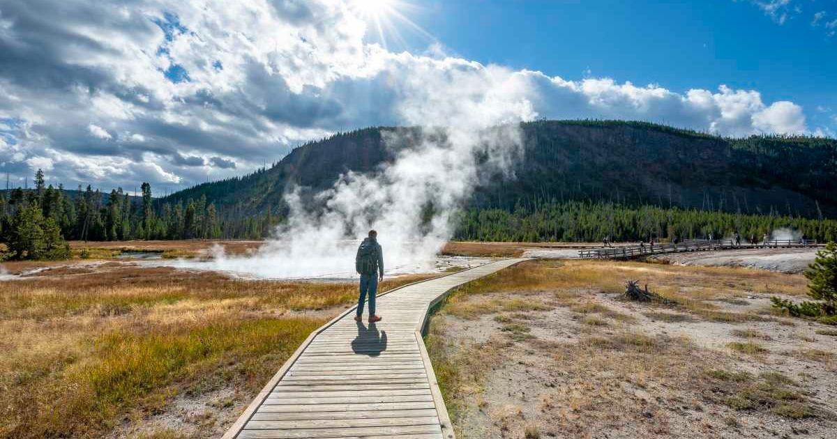 A tourist walks in front of a steaming hot spring in Yellowstone National Park (Representative Cover Image Source: Getty Images | Photo by imageBROKER | Mara Brandl)