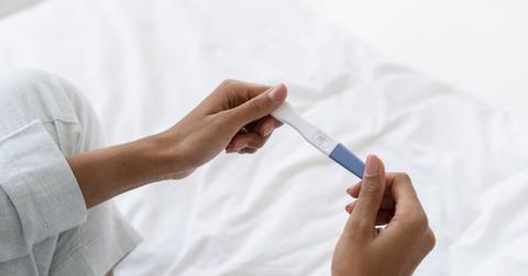 Woman sitting on white sheet holding a pregnancy test
