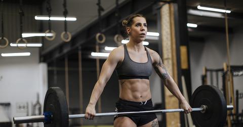 A woman wearing a sports bra holds a barbell at her waist while working out.