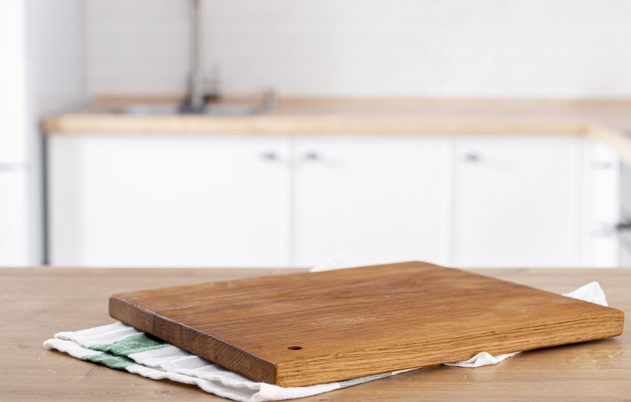 A wooden cutting board rests atop a kitchen towel to dry.