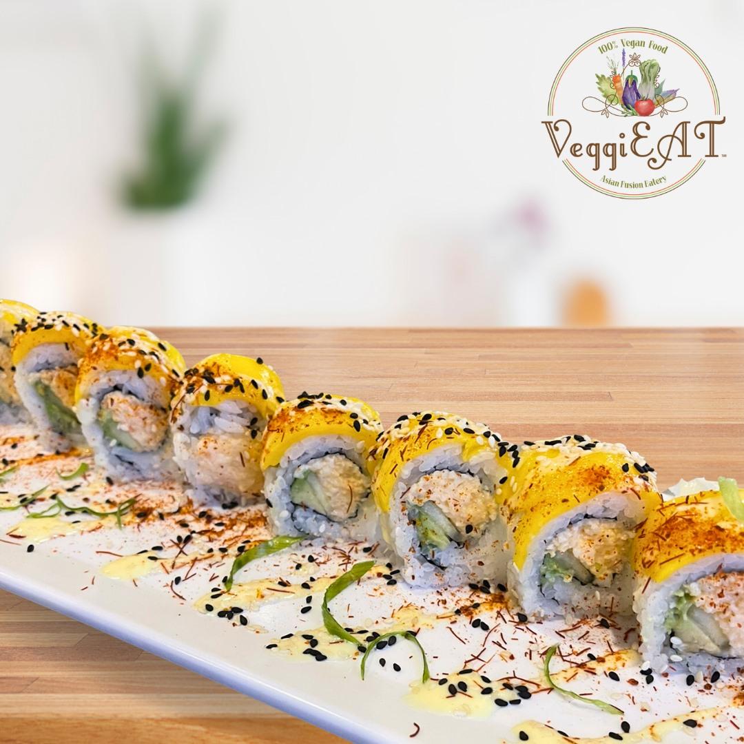 Vegan sushi topped with mango is featured on a plate atop a wooden table.