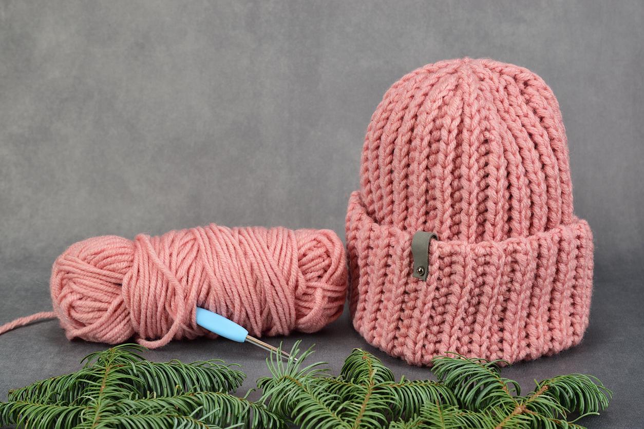 Completed pink crochet beanie next to the hook and yarn used for the project.