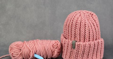 Completed pink crochet beanie next to the hook and yarn used for the project.