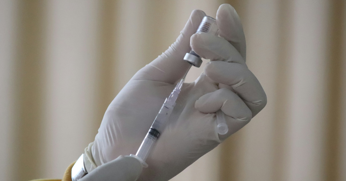 A gloved hand draws a vaccine into a syringe 