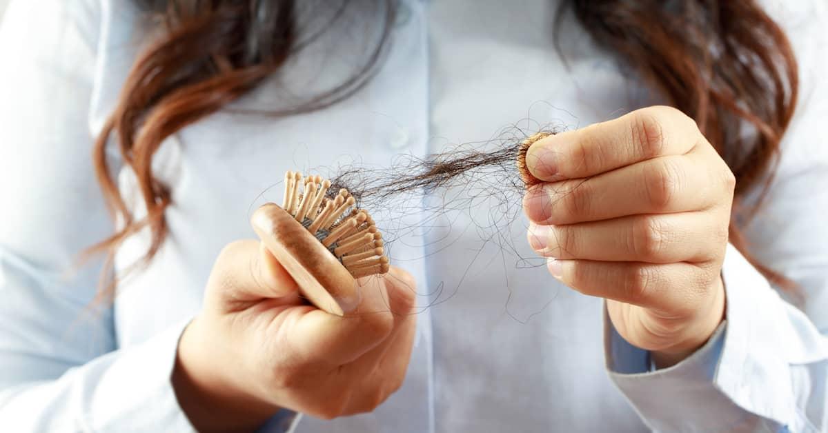 Close-up shot of a person with long hair pulling a clump of hair out of a brush. 