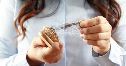 Close-up shot of a person with long hair pulling a clump of hair out of a brush.