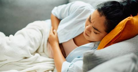 Young Asian person lying on a sofa, in pain and holding their abdomen