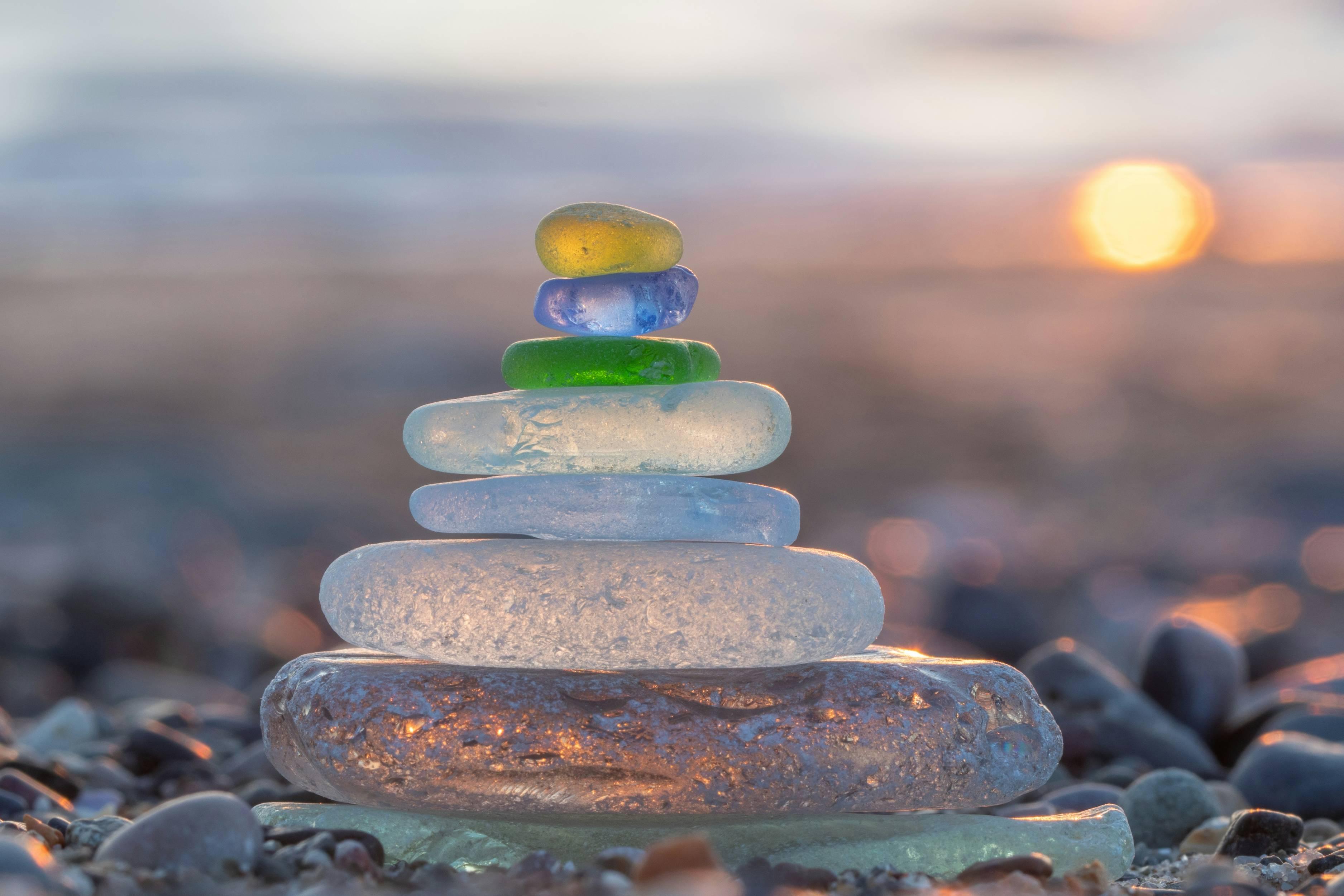 Sea glass that has been frosted and rounded is stacked atop one another in front of a sunset.