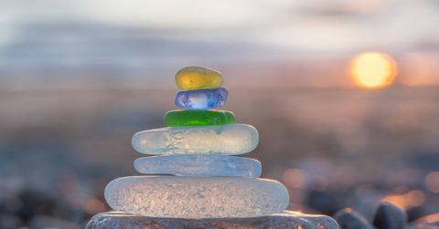 Sea glass that has been frosted and rounded is stacked atop one another in front of a sunset.