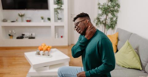 A man in a green sweater sitting on a couch cracks his neck.