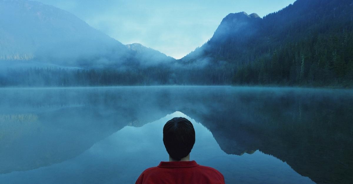 Back of man's head looking at a lake with mountains in the distance on a foggy day