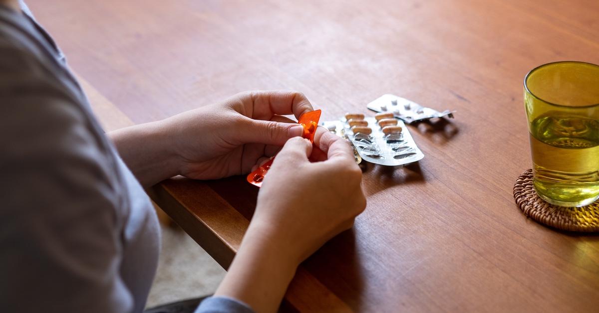 Woman taking decongestant tablets at a table with a glass of water.