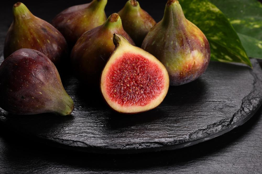 A bunch of figs on a black setting with one in the front cut in half. 