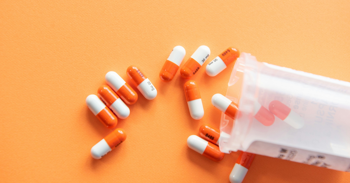 Orange and white pills are spilled from a prescription pill bottle