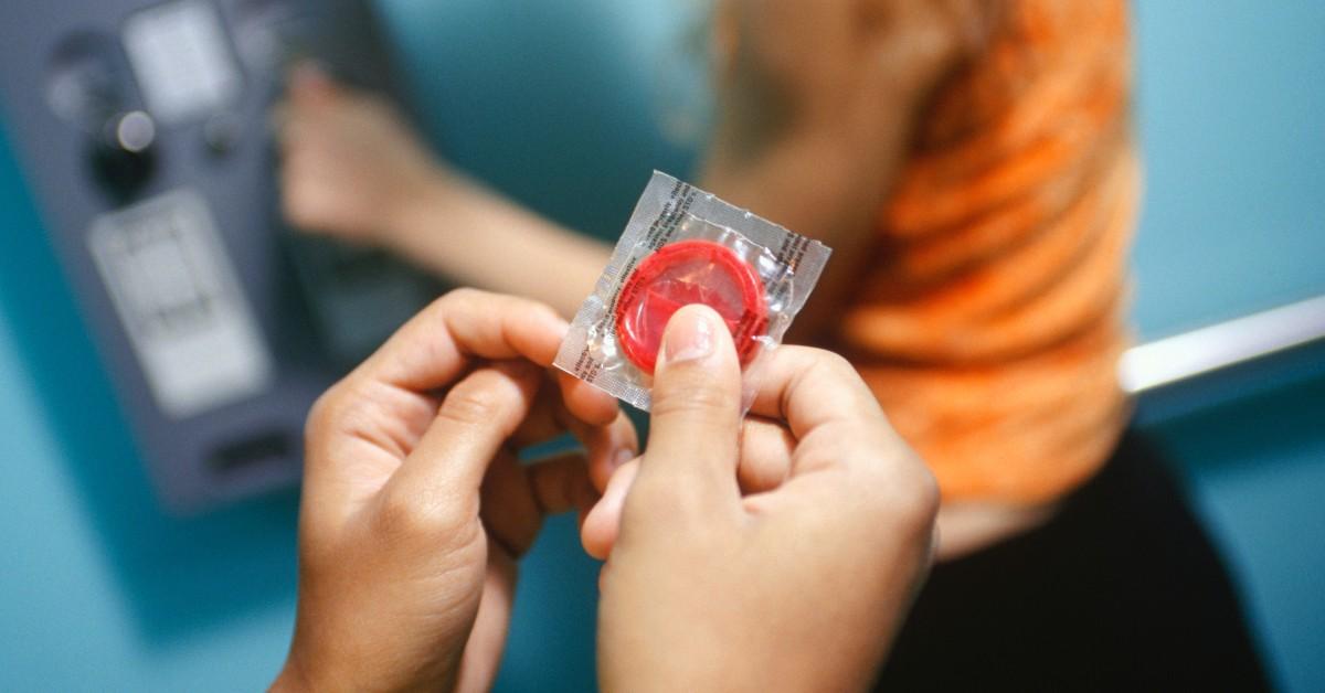 A person holds a red condom in their hands