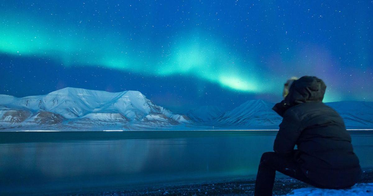 A man sitting on an icy landscape looking at the aurora borealis. (Representative Cover Image Source: Pixabay | Noel_Bauza)