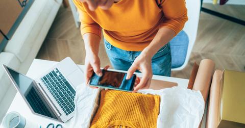 A woman in an orange top takes a photo with her phone of a yellow sweater to sell online.