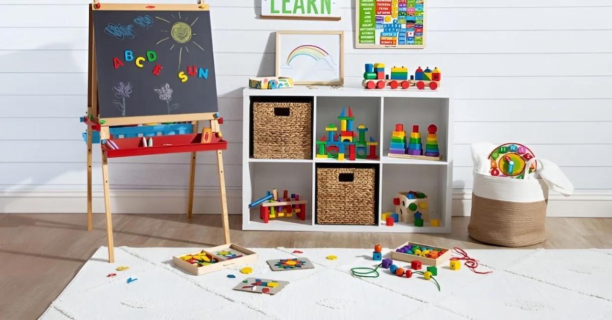 Against the wall of a playroom sits a chalkboard easel, and various rainbow colored toys on the floor and in shelves