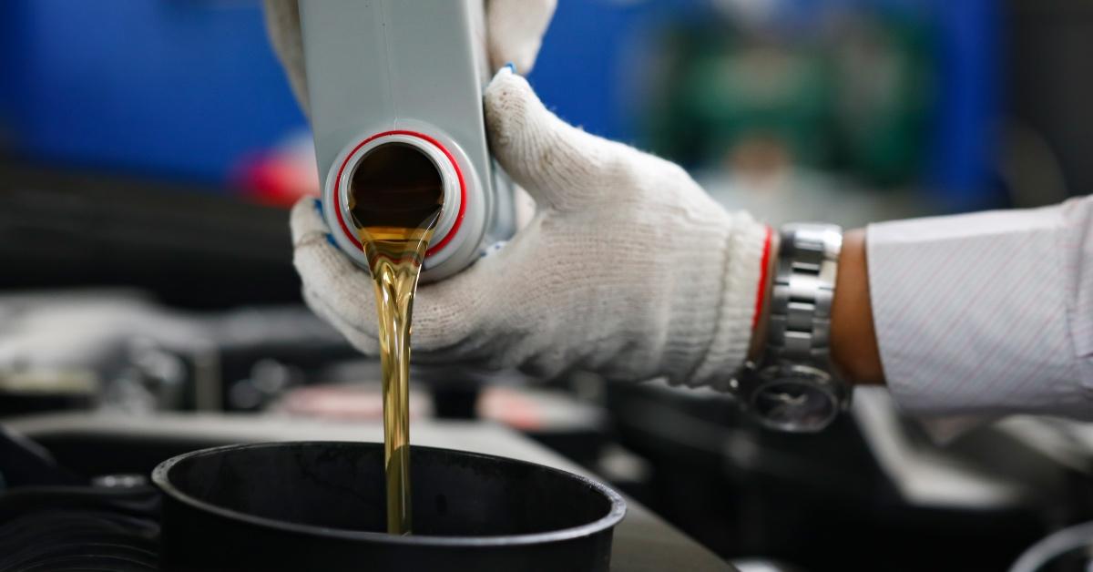 Person wears gloves to pour oil in to a car engine. 