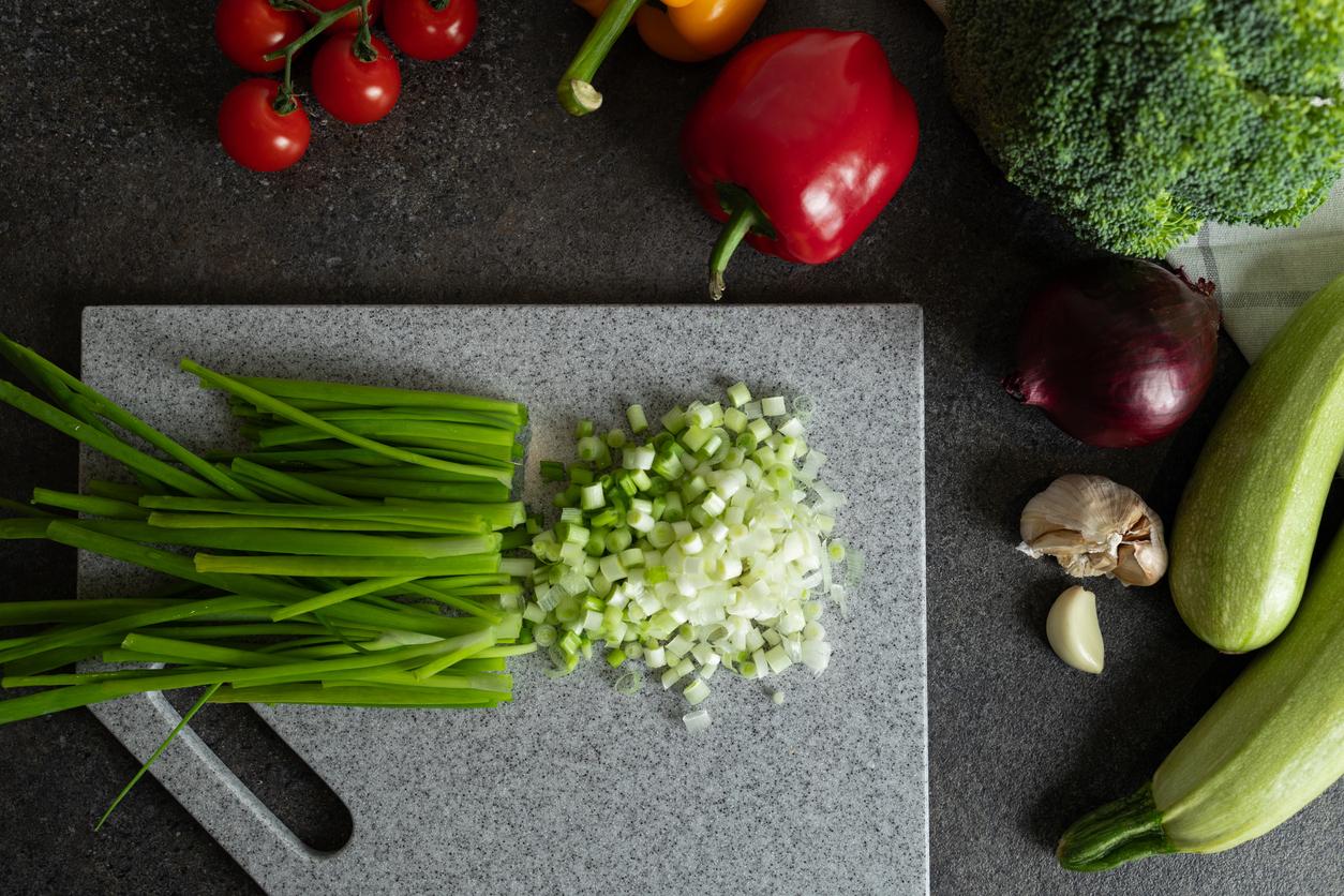 A bunch of clean green onions chopped halfway on a gray cutting board surrounded by other random vegetables.