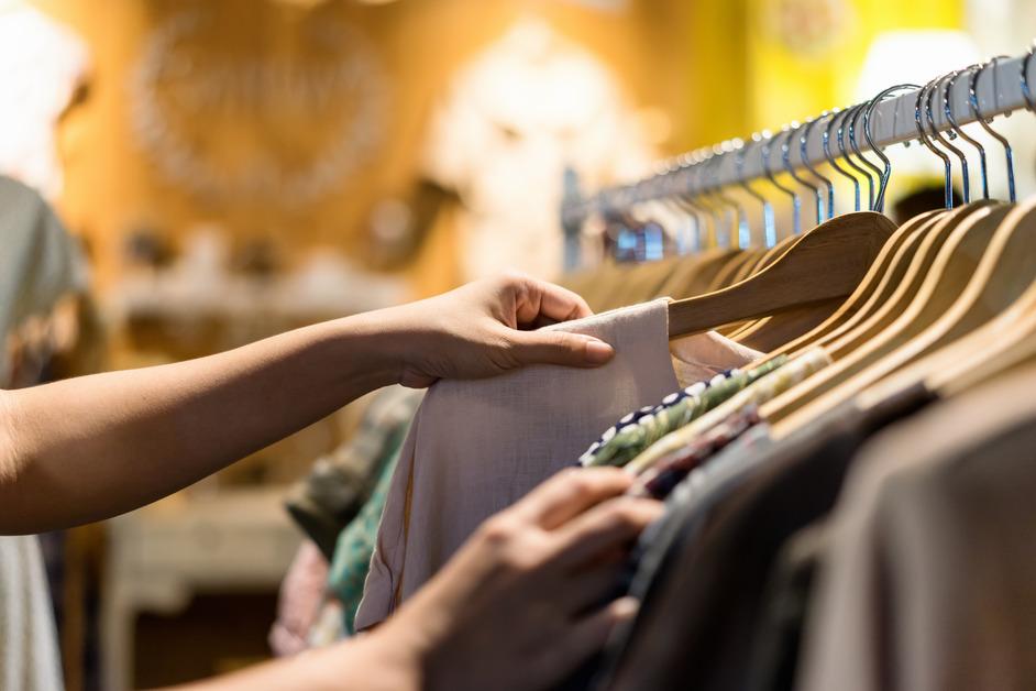 Woman pulling a shirt off the rack at a thrift store. 