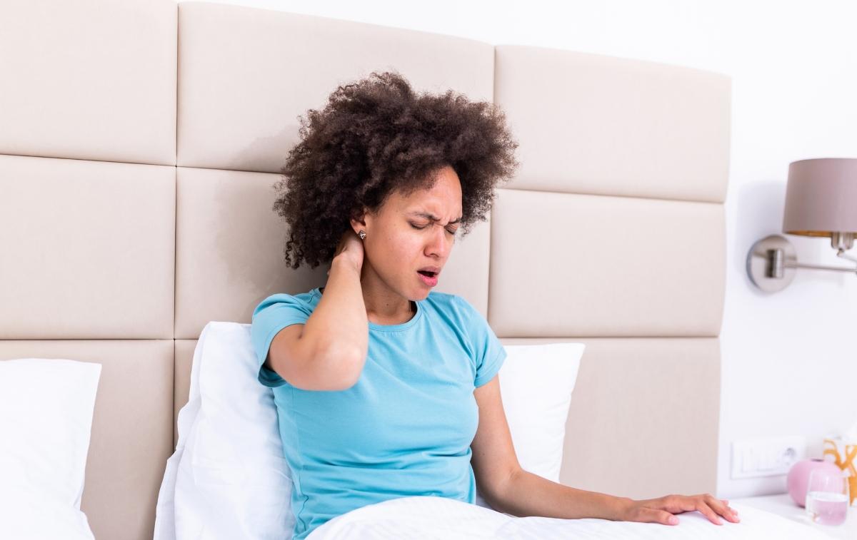 Black woman sitting in bed rubbing her neck