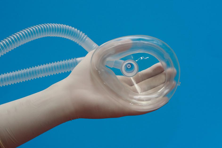 A hand holding a medical gas mask in front of a blue background. 