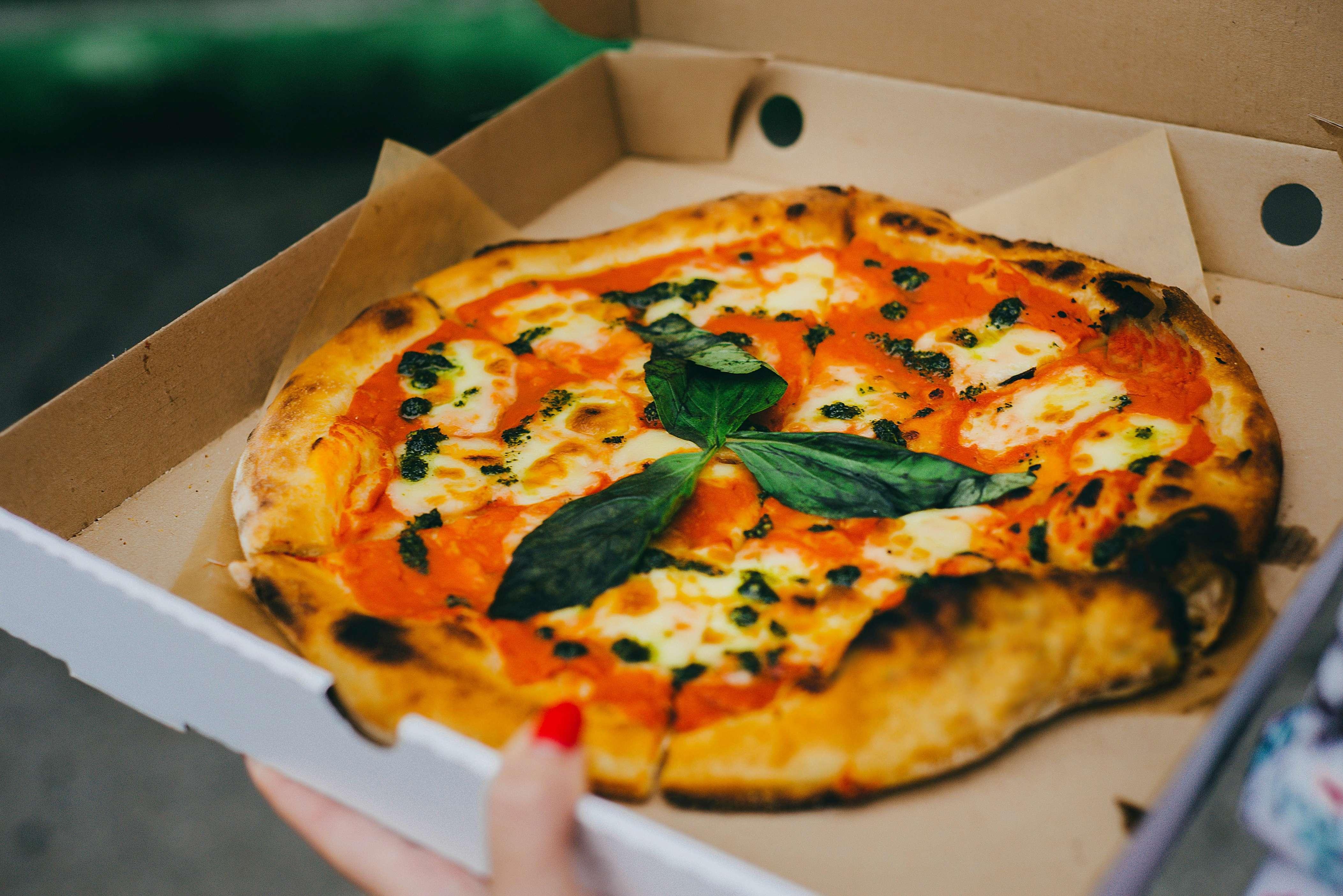 A close-up photo of a pizza in a cardboard takeout box.