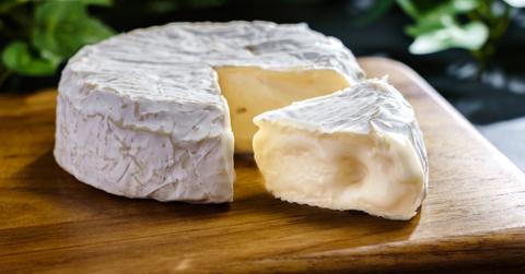 A photo of brie cheese sitting on a wooden cutting board.