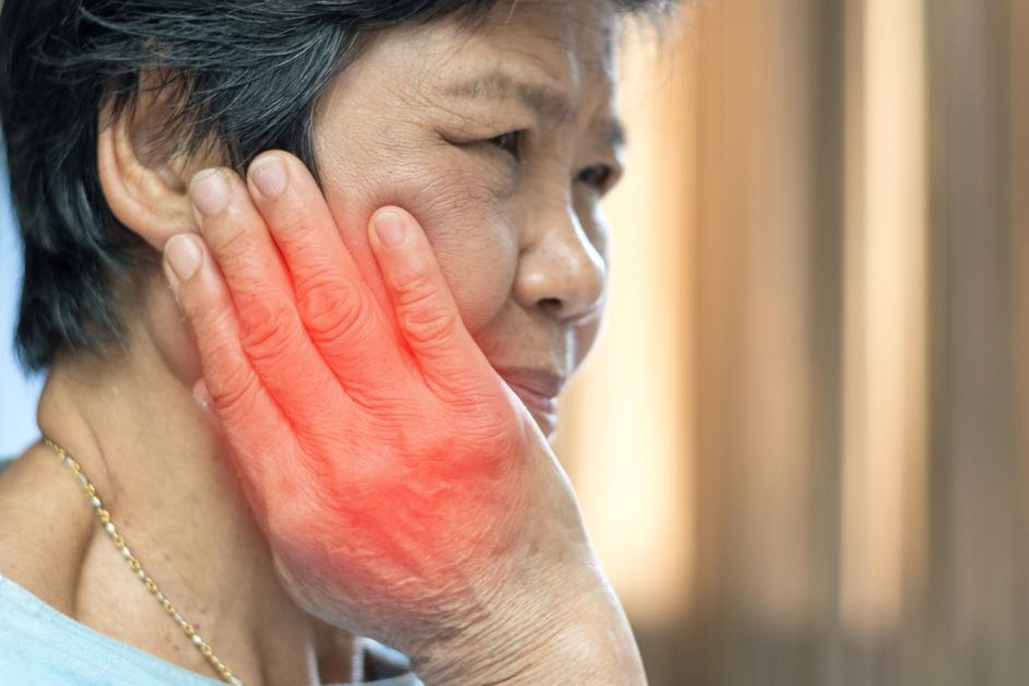 An older woman holds the side of her face with a red glow to emphasize pain. 