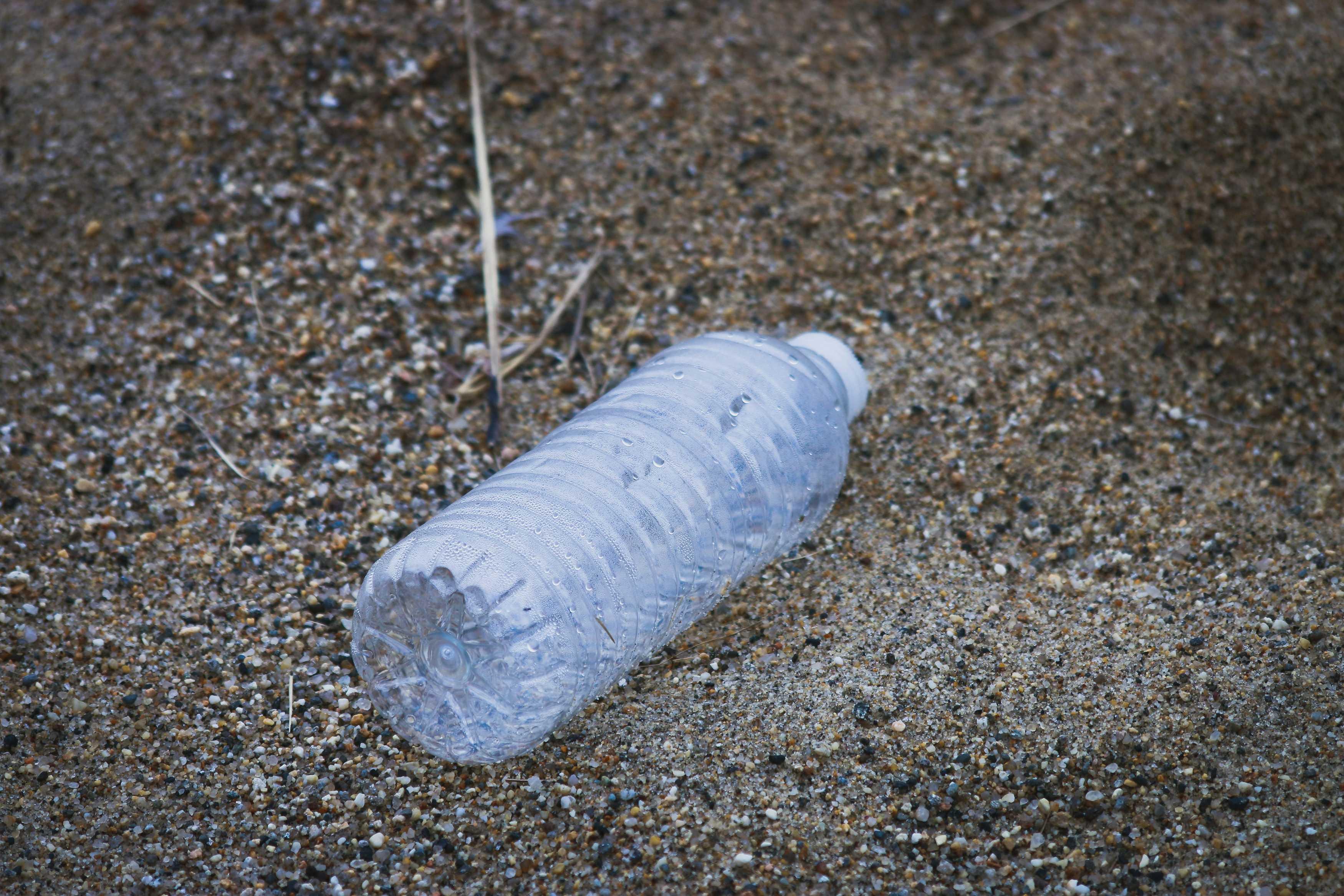 A plastic water bottle appears empty, laying atop gravel.