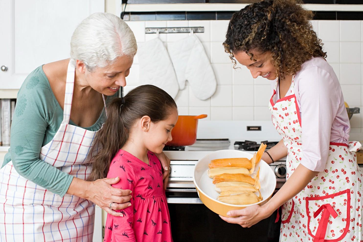 Three generations of a family prepare tamales together in a kitchen.