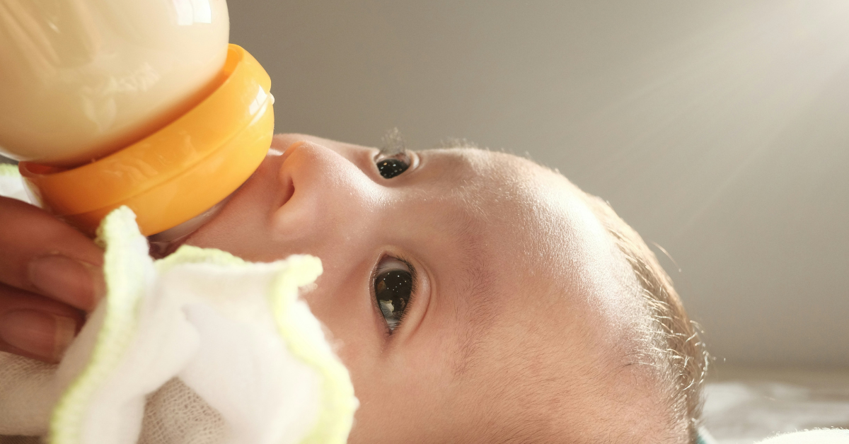 A closeup of a baby drinking formula out of a bottle