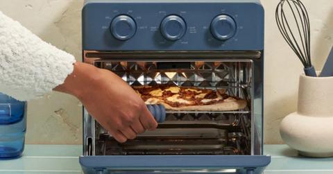 person pulling pizza our of blue air fryer