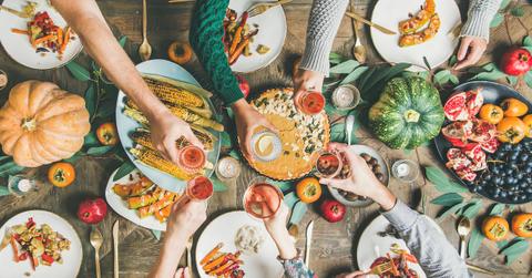 Over a dinner table covered in plates of food, various hands hold glasses in a toast, from a top view.