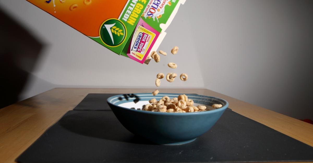 A photo of someone pouring Cheerios into a blue bowl on a table. 