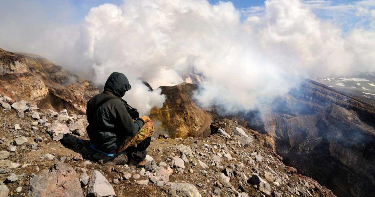 A person sitting on a mountain top watching plumes of smoke from a volcano waking up. (Representative Cover Image Source: Getty Images | Yevgen Timashov)