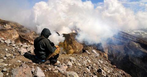 A person sitting on a mountain top watching plumes of smoke from a volcano waking up. (Representative Cover Image Source: Getty Images | Yevgen Timashov)
