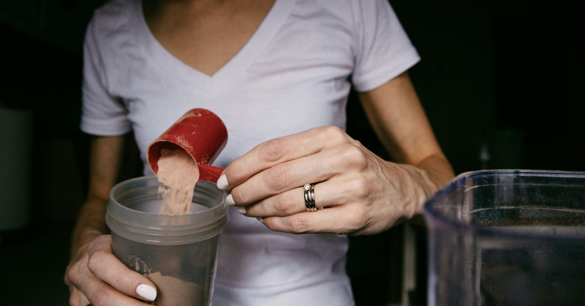 A woman dumps a scoop of protein powder into a shaker