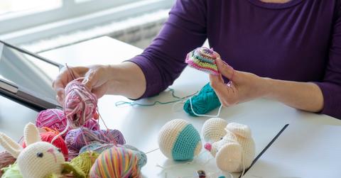 Person working on a multi-colored crochet project while surrounded by yarn and other supplies.
