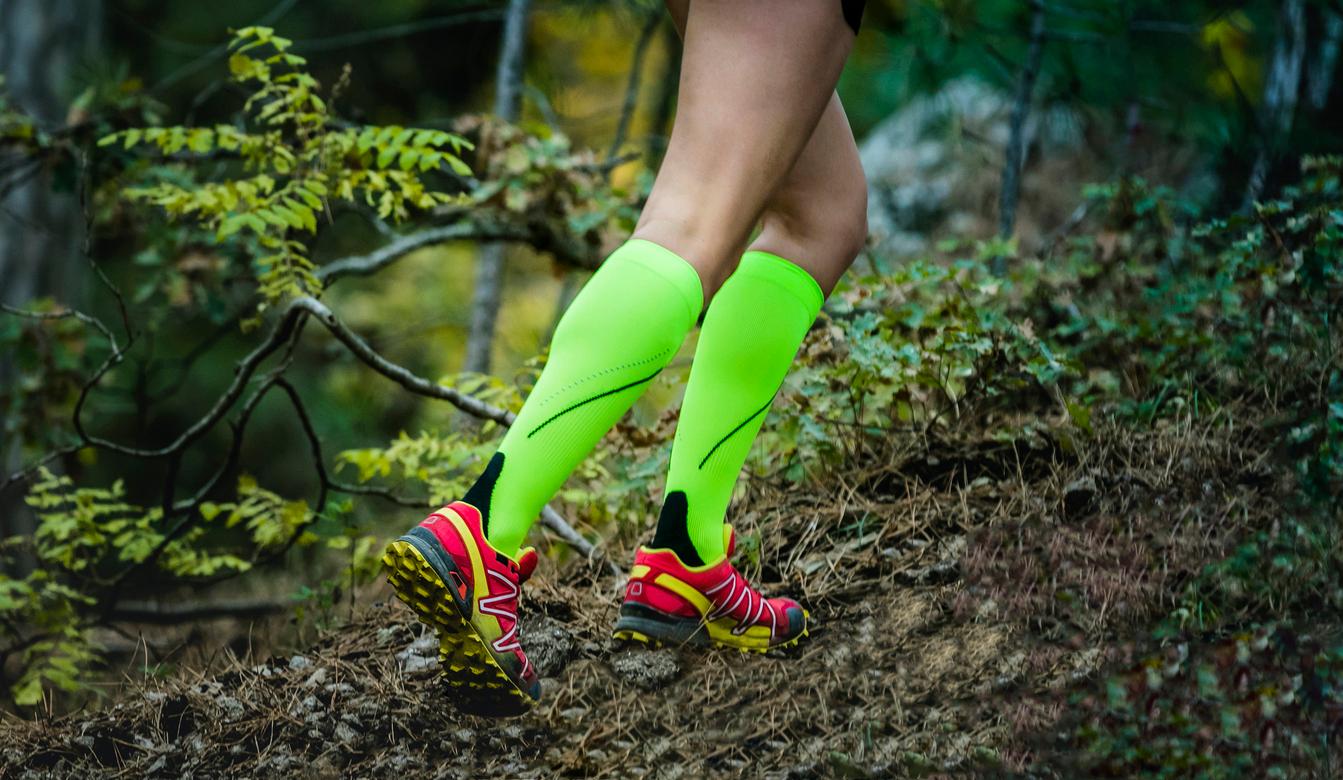 A person appears running on a woodsy trail while wearing yellow-green compression socks.