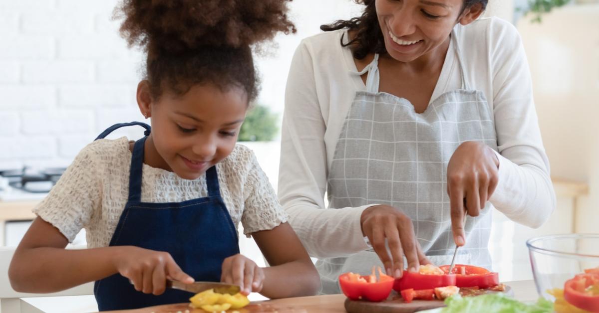 A mother and daughter cutting vegetables together. 