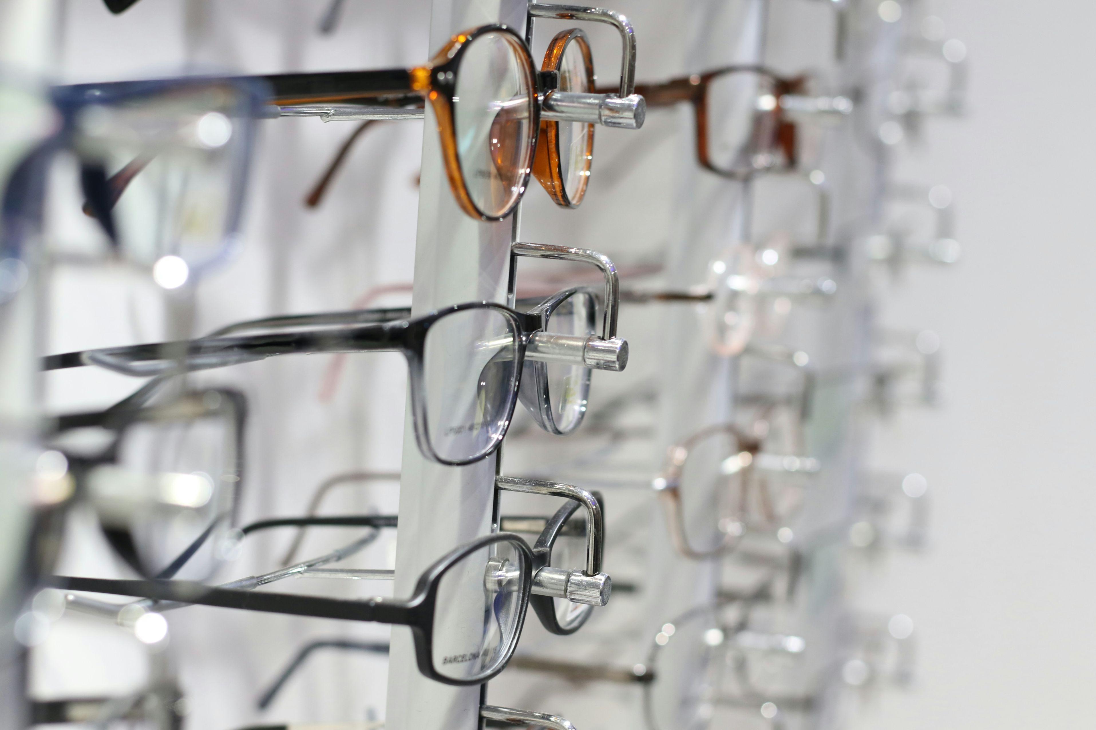 Several pairs of eyeglasses with different designs and sizes are pictured on racks in a doctor's office.