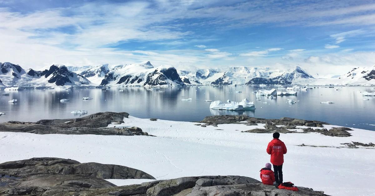 Two people in red jackets look out at the icy tundra of Antarctica 