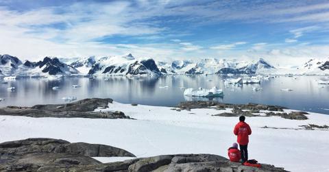 Two people in red jackets look out at the icy tundra of Antarctica