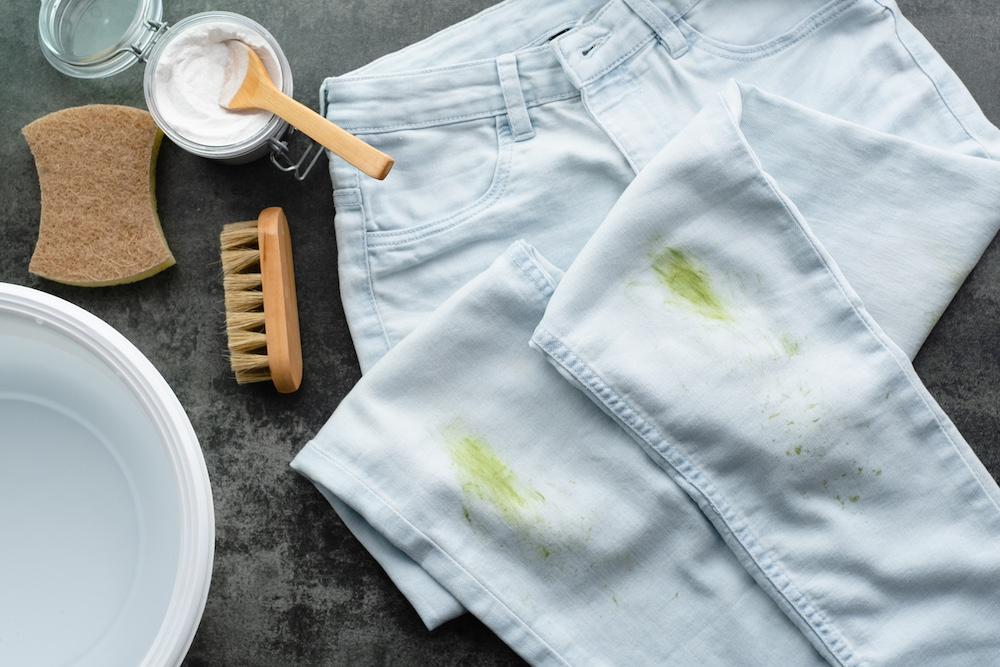 A pair of light-wash jeans with grass stains next to stain-treating products. 