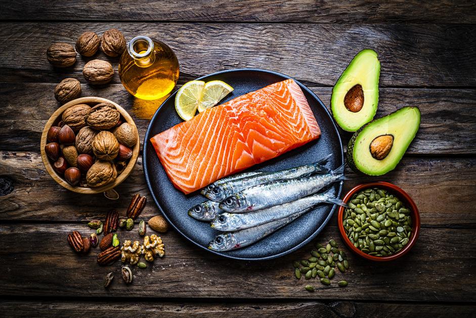 An assortment of omega-3 fatty acid sources, such as salmon, avocado, walnuts, pumpkin seeds, all gathered on a table. 