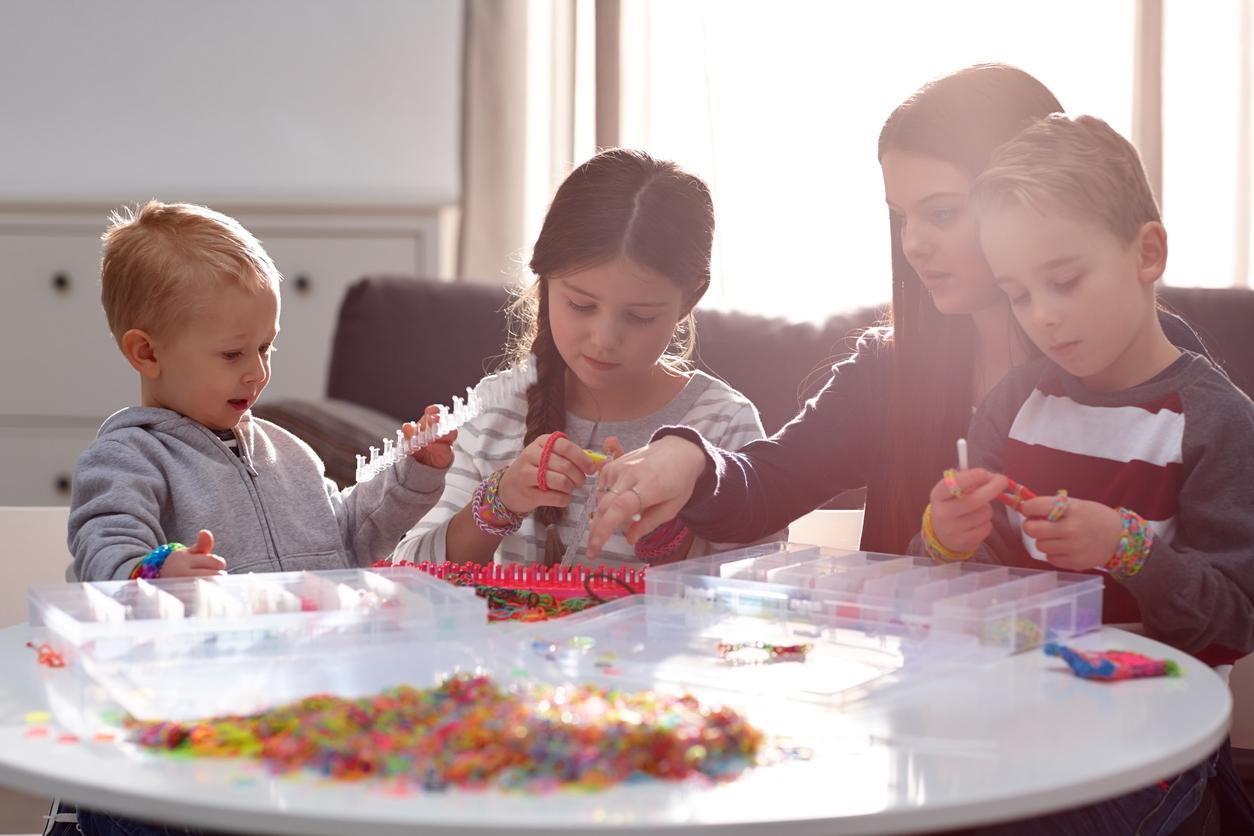 A family of young children make bracelets together with an adult at a white table.