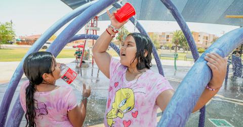 Two young girls play in a playground and one pours water on her head from a red cup