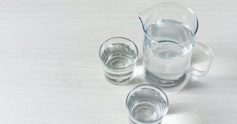 A pitcher with two glasses of water sit on a gray background